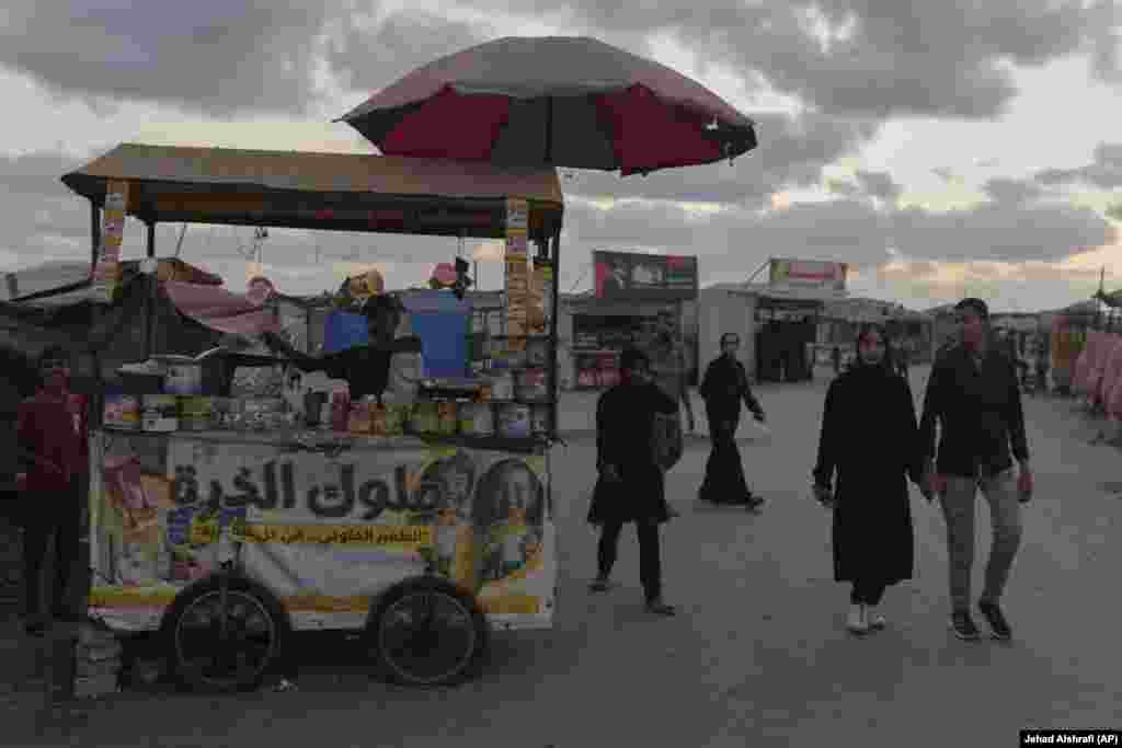 Një çift palestinez duke kaluar pranë një tezge ushqimore.