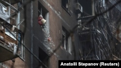 Мешканка житлового будинку викидає розбите скло з вікон без шибок своєї квартири у Краматорську після удару російського безпілотника, грудень 2025 року