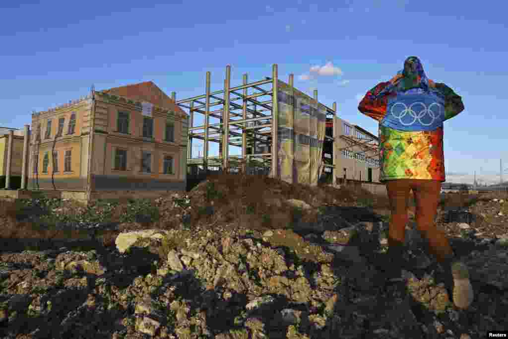 A volunteer walks past a construction site with an unfinished building under a cover decorated with drawings of windows in Sochi, Russia, on February 6. (Reuters/Eric Gaillard)