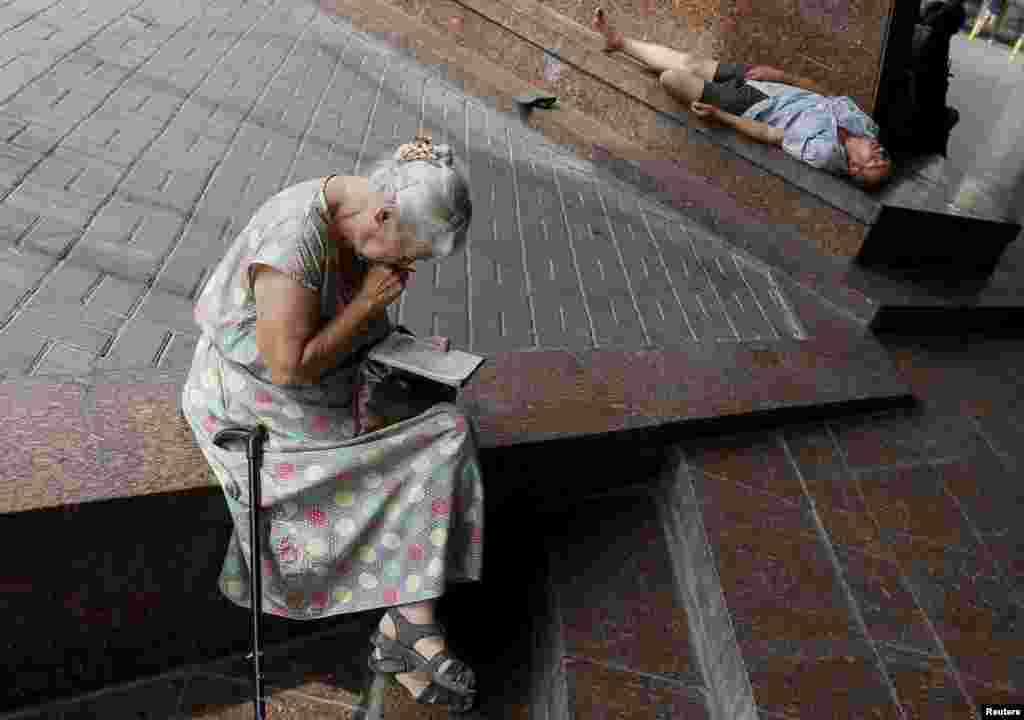 An elderly woman works on a crossword puzzle as she rests in the shade during a heatwave in central Kyiv. (Reuters/Gleb Garanich)