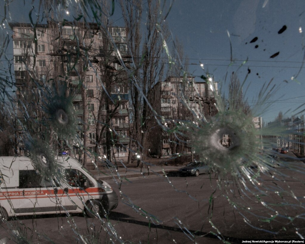 Крізь пошкоджене пострілами вікно автомобіля видно карету швидкої допомоги. Києв, Україна. 28 лютого 2022 року