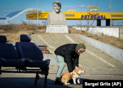Un localnic se joacă cu un câine în fața unei statui a fostului lider sovietic Vladmir Lenin, în Comrat, Moldova, 12 martie 2022.
