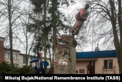 Bărbații din localitate urmăresc cum un monument al armatei sovietice din anii 1940 este scos din soclu la Sieldce, la 90 de kilometri est de Varșovia, pe 20 aprilie.