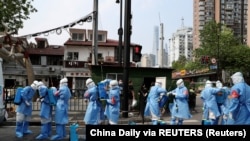 Punëtorët shëndetësorë duke u përgatitur për të dezinfektuar një ndërtesë në Shangai.