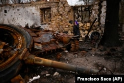 O femeie stă lângă un tanc rusesc distrus. Imagine din nordul Ucrainei, orașul Cernigău, 23 aprilie 2022. AP Photo/Francisco Seco