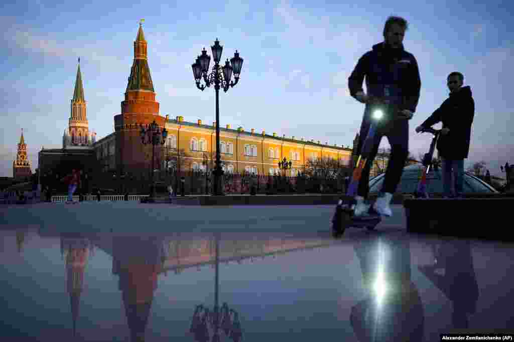 Young people ride scooters in Manezhnaya Square near Red Square and the Kremlin after sunset in Moscow.