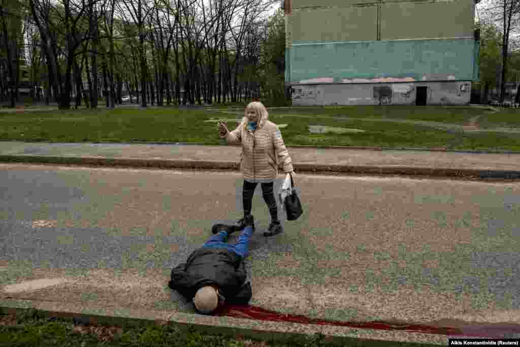 Харков, 19-уми апрели 2022. Як зан дар паҳлӯи ҷасади марде, ки ҳангоми тирборон дар маҳаллаи истиқоматӣ кушта шудааст.