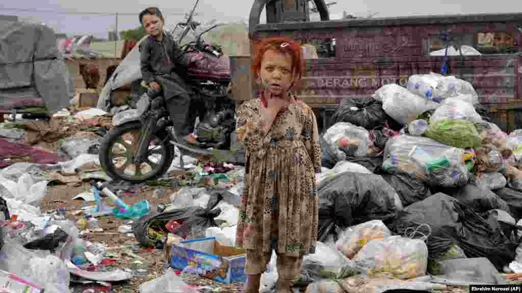 Two Afghan children stand amid piles of garbage next to their home in Kabul. Afghanistan&rsquo;s gross domestic product is hard to measure, but it is estimated to have dropped by nearly 20 percent since the Taliban returned to power, endangering the lives of millions in an already impoverished country. &nbsp;