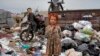 Two Afghan children stand amid piles of garbage next to their home in Kabul.&nbsp;