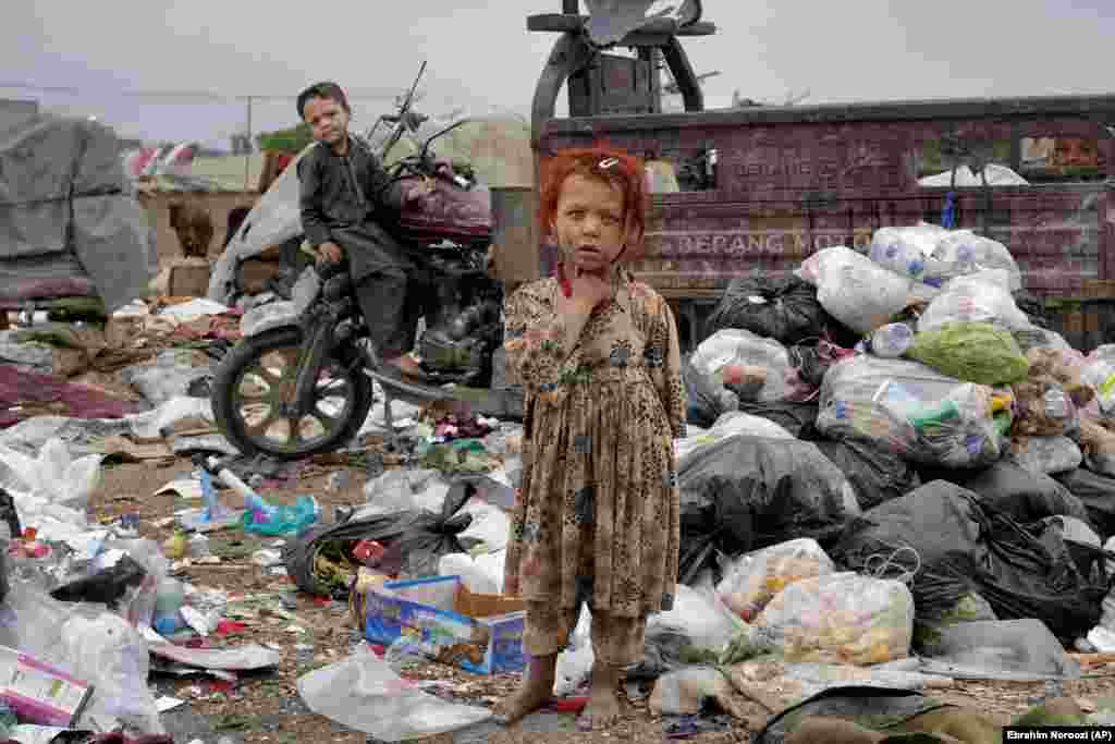 Two Afghan children stand amid piles of garbage next to their home in Kabul.&nbsp;