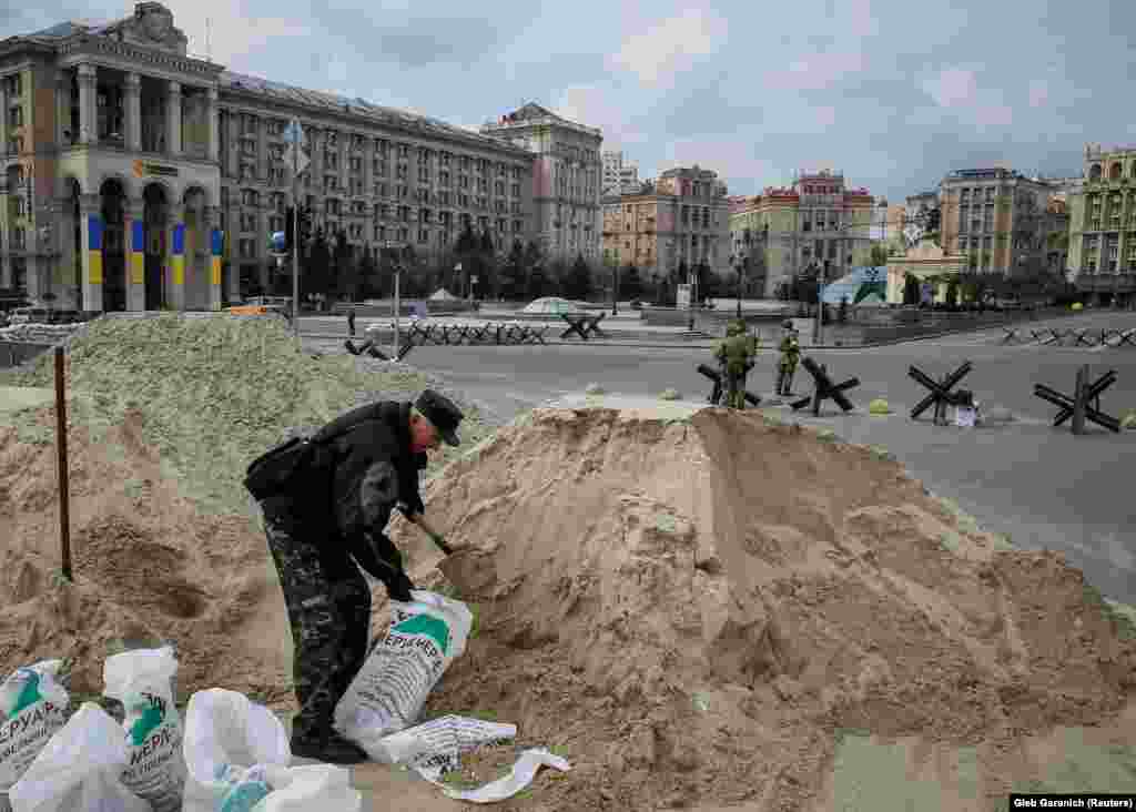 A man fills sandbags in the center of Kyiv on March 7 as volunteers from the Territorial Defense Forces patrol in the background.&nbsp;