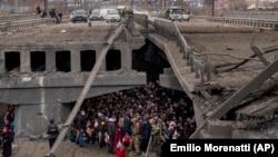 Ukrainians fleeing the fighting crowd under a destroyed bridge as they try to cross the Irpin River in the outskirts of Kyiv.