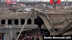  Украински жители пробват да преминат под съборен от въздушни удари мост в градчето Ирпин на северозапад от Киев. 5 март, 2022. 