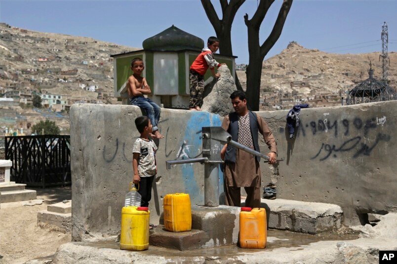 Një burrë me fëmijët e tij duke mbledhur ujë nga një pompë publike uji në Afganistan.