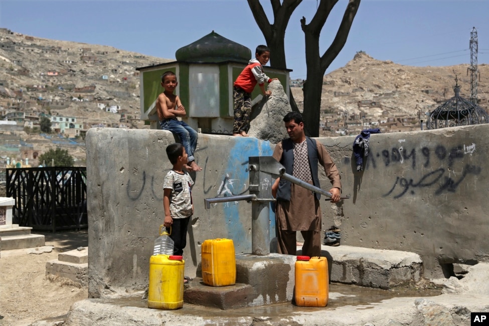 Një burrë me fëmijët e tij duke mbledhur ujë nga një pompë publike uji në Afganistan.