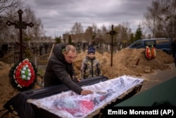 A boy looks at the body of his mother lying in a coffin as his father prays during her funeral in Bucha, on the outskirts of Kyiv, on April 20.
