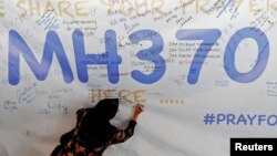 Женщина оставляет надпись на баннере в поддержку пассажиров самолета "Боинг-777", выполнявшего рейс MH370 из Куала-Лумпура в Пекин. 12 марта 2014 года.