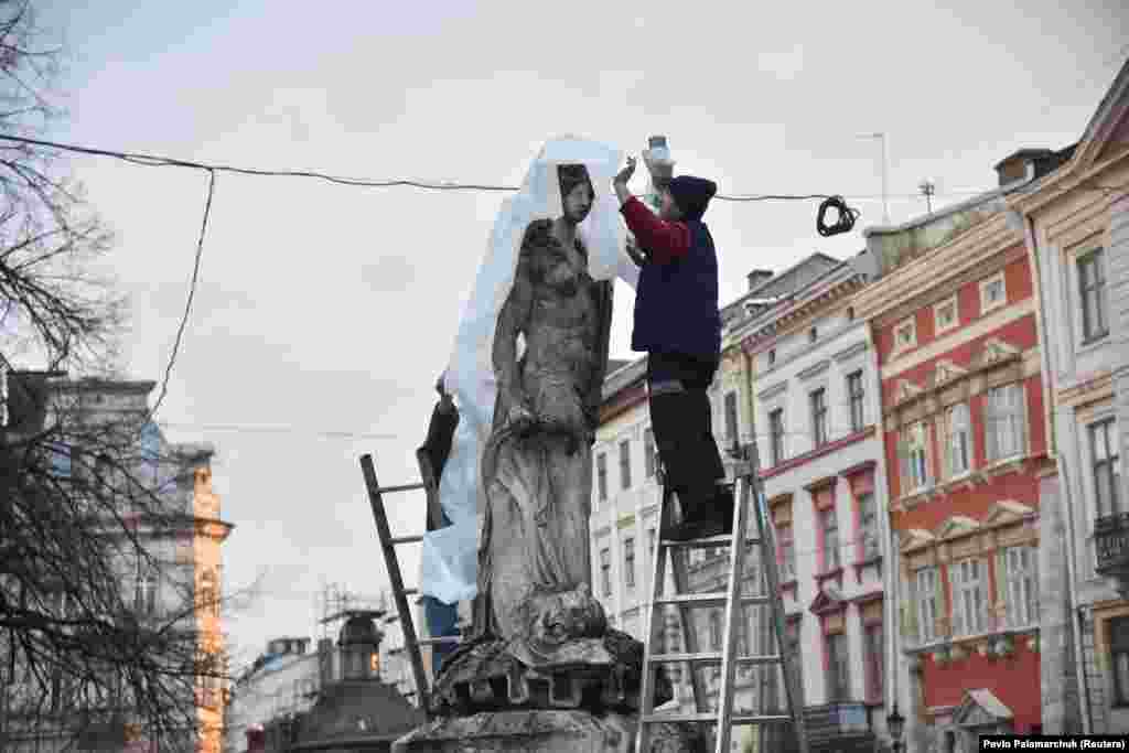 Рабочыя і валянтэры абгортваюць скульптуры на галоўнай плошчы Львова