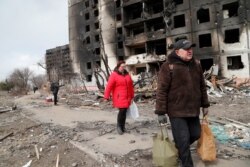Ljudi hodaju u blizini stambenih blokova, koji su uništeni tokom ruske invazije na opkoljeni lučki grad Mariupolj, 17. marta 2022.
