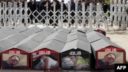 People gather next to symbolic coffins with pictures of Syrian victims and inscriptions that translate as "killer Assad" and "killer Putin" during a protest against Russia for its alleged role in a chemical attack in the Syrian province of Idlib on April 7.