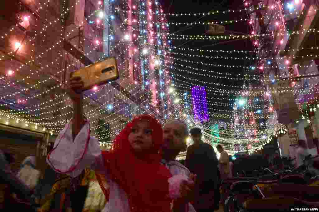 Një vajzë e vogël shkrep një selfie së bashku me vëllanë e saj në rrugët e ndriçuara në Karaçi të Pakistanit, ku është festuar ditëlindja e Profetit Muhamed.(AFP/Asif Hassan)