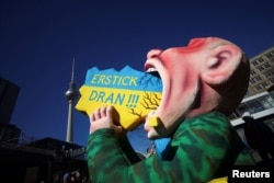 Caricatura lui Putin devorând Ucraina, marca Tilly, a luat parte la carnavalul din Berlin la doar câteva zile după declanșarea invaziei pe scară largă, anume pe 13 martie 2022. Textul în germană: „Sta-ți-ar în gât!”