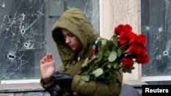Një grua duke kaluar pranë një dritareje të dëmtuar, rrugës për të vendosur lule në një memorial të improvizuar për viktimat e granatimeve të fundit në qytetin e Donetsk në Ukrainë, të kontrolluar nga separatistët, 15 mars 2022.