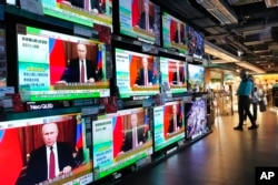 Люди стоять біля екранів телевізорів у Гонконзі, що транслюють новини про атаку Росії на Україну 24 лютого 2022 року