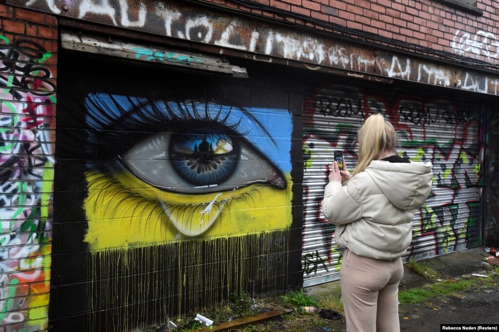 Një grua duke fotografuar një mural të një syri të përlotur, me ngjyrat e flamurit të Ukrainës, të realizuar nga artisti "MyDogSighs", në Kardif, Uells, Britani, më 2 mars.