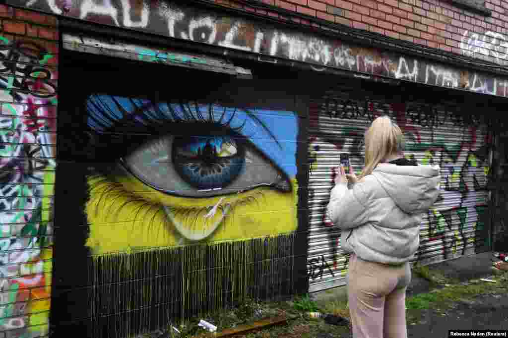 Žena fotografiše mural koji pokazuje oko sa suzom u bojama ukrajinske zastave uličnog umjetnika sa imenom &quot;MyDogSighs&quot;, u Cardiffu, Wales, Velika Britanija, 2. mart 2022.