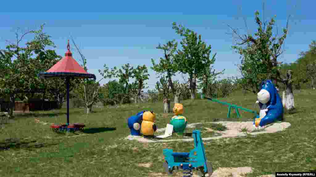 Мультяшный ослик Иа на детской площадке в старом черешневом саду перед фермой
