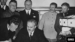 Ministrul de externe sovietic Viaceslav Molotov semnează pactul de neagresiune, sub privirile lui Ribbentrop și Stalin.