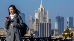 A woman looks at her phone as she walks across a bridge with the Russian Foreign Ministry building in the background, in central Moscow. (file photo)