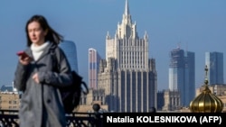 A woman looks at her phone as she walks across a bridge with the Russian Foreign Ministry building in the background, in central Moscow. (file photo)