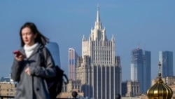 Жена гледа телефона си, докато върви по мост в центъра на Москва, на фона на сградата на руското външно министерство (илюстративна снимка).