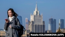 Жена гледа телефона си, докато върви по мост в центъра на Москва, на фона на сградата на руското външно министерство (илюстративна снимка).