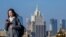 Жена гледа телефона си, докато върви по мост в центъра на Москва, на фона на сградата на руското външно министерство (илюстративна снимка).