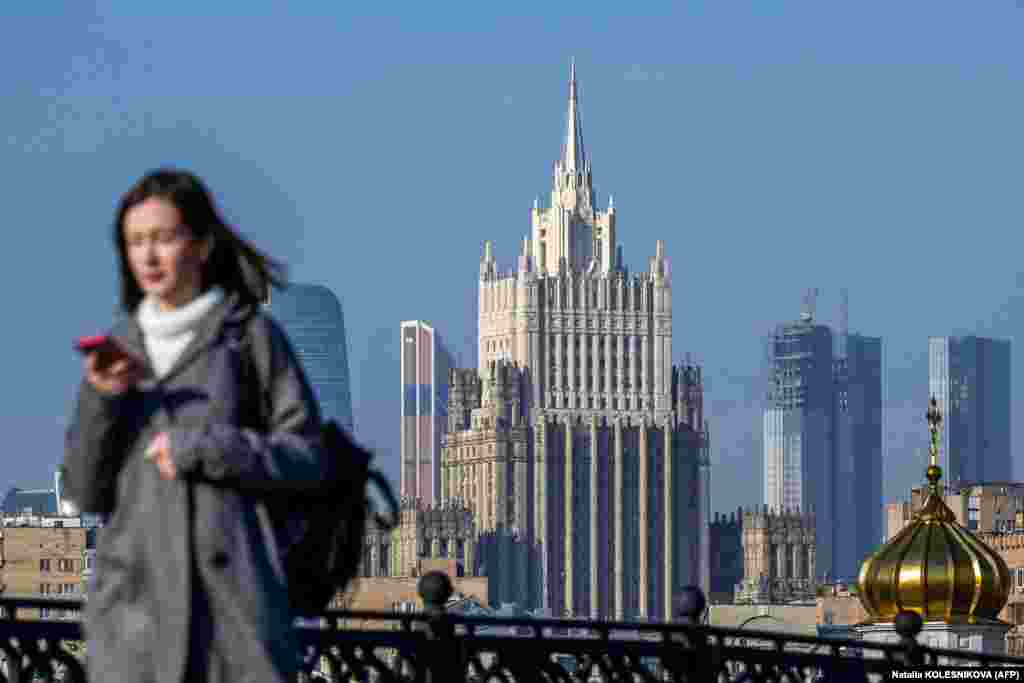 A woman looks at her phone as she walks across a bridge with the Russian Foreign Ministry building in the background in central Moscow on October 12.&nbsp;