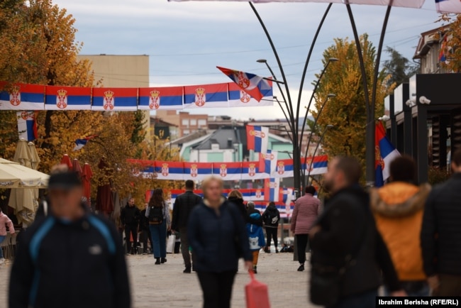 Prolaznici ispod zastava Srbije na glavnom trgu u Severnoj Mitrovici.