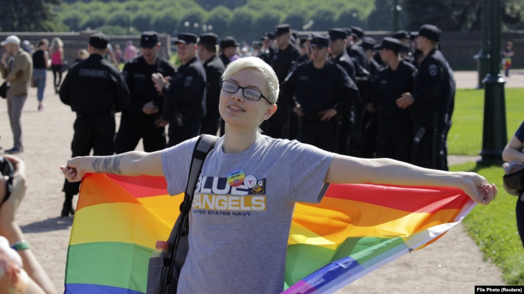 A participant poses with a rainbow flag with Interior Ministry officers in the background during an LGBT rally in St. Petersburg in 2017.