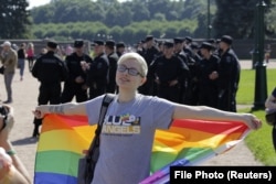 Učesnik koji drži zastavu duginih boja pozira za fotografiju ispred službenika Ministarstva unutrašnjih poslova tokom LGBT skupa u St. Petersburgu 2017.