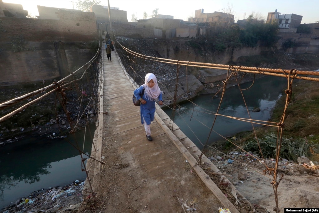 Një nxënëse, dhe disa persona më larg saj, shihen duke kaluar një urë të improvizuar në Peshavar të Pakistanit.