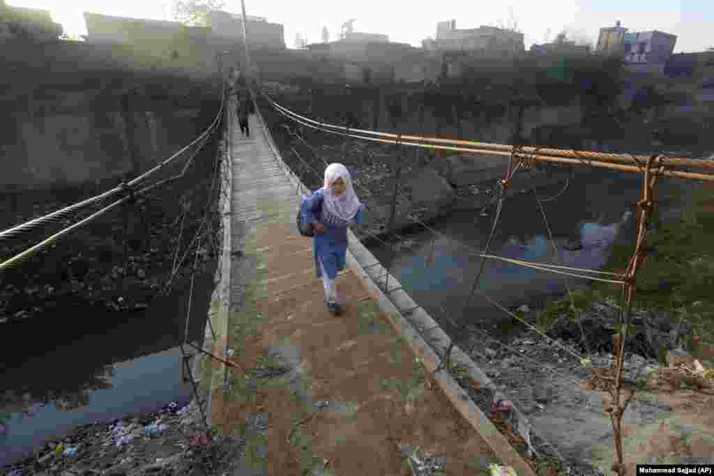 A student and others cross a makeshift bridge set up on a stream near a slum area of Peshawar, Pakistan.