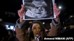 Një grua mban lart një ekografi fetale më 1 dhjetor 2022 në Prishtinë, ndërsa merr pjesë në një protestë kundër dhunës ndaj grave në Kosovë, i thirrur pas vrasjes së një gruaje shtatzënë nga ish-burri i saj në maternitetin ku ajo do të lindte.