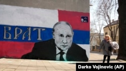 Një grua duke kaluar pranë një murali me portretin e presidentit rus, Vladimir Putin, dhe mbishkrimin "vëlla"(brat).