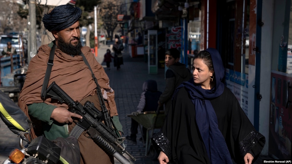 A Taliban security officer stands guard on a Kabul street as a woman passes by. (file photo)