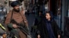 A Taliban fighter security officer stands on duty as a woman walks past him in Kabul. (file photo)