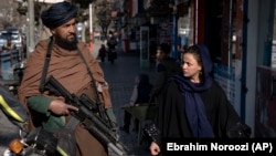 Egy tálib harcos áll szolgálatban, miközben egy nő elsétál mellette Kabulban