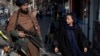 A Taliban fighter security officer stands on duty as a woman walks past him in Kabul. (file photo)