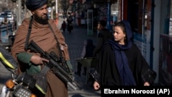 A Taliban fighter security officer stands on duty as a woman walks past him in Kabul. (file photo)